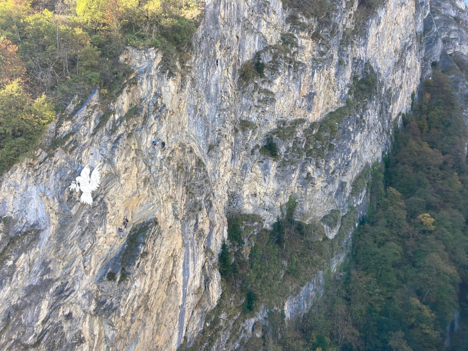 Unter der Vogelskulptur sind auf dem Klettersteig Farinetta ganz klein Menschen zu sehen.